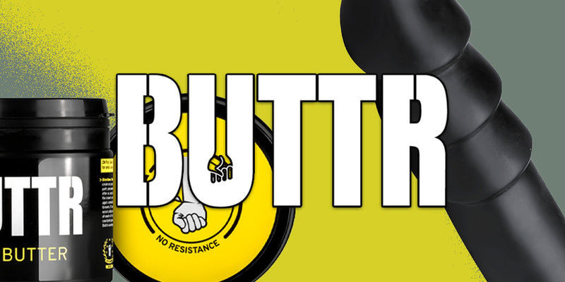 Promotional graphic for BUTTR Butter featuring a black tub of butter on the left, a black cylindrical container on the right, and a yellow circular badge with a fist logo in the center, set against a bright yellow background with large white 'BUTTR' text.