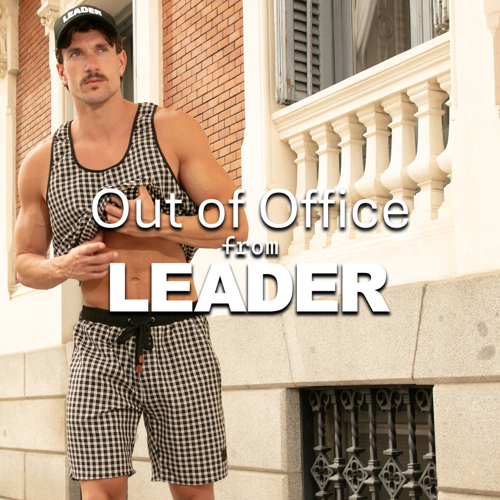 Man wearing a checkered tank top and shorts with text 'Out of Office from LEADER' on a building background