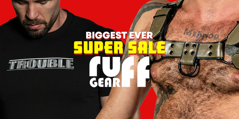 Promotional graphic for Ruff Gear featuring a man in a black T-shirt with 'TROUBLE' printed on it, alongside a close-up of a leather harness worn by another man, set against a solid red background with large text reading 'BIGGEST EVER SUPER SALE' and 'RUFF GEAR'.